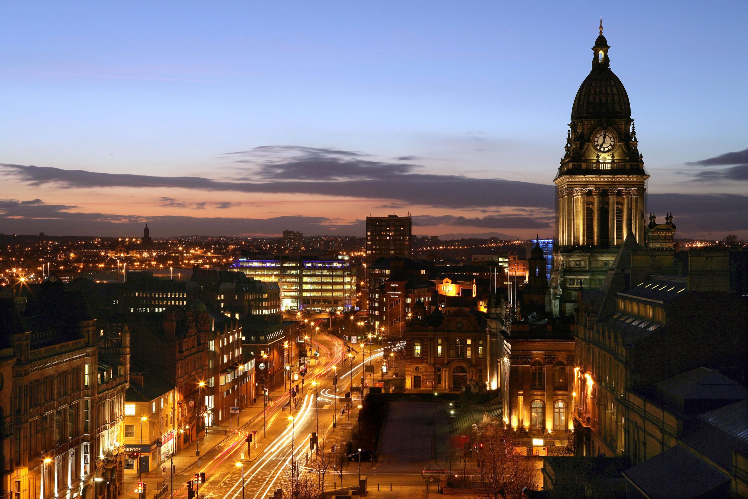 An image of the city scape of Leeds city centre at night with bright lights from an aerial point of view