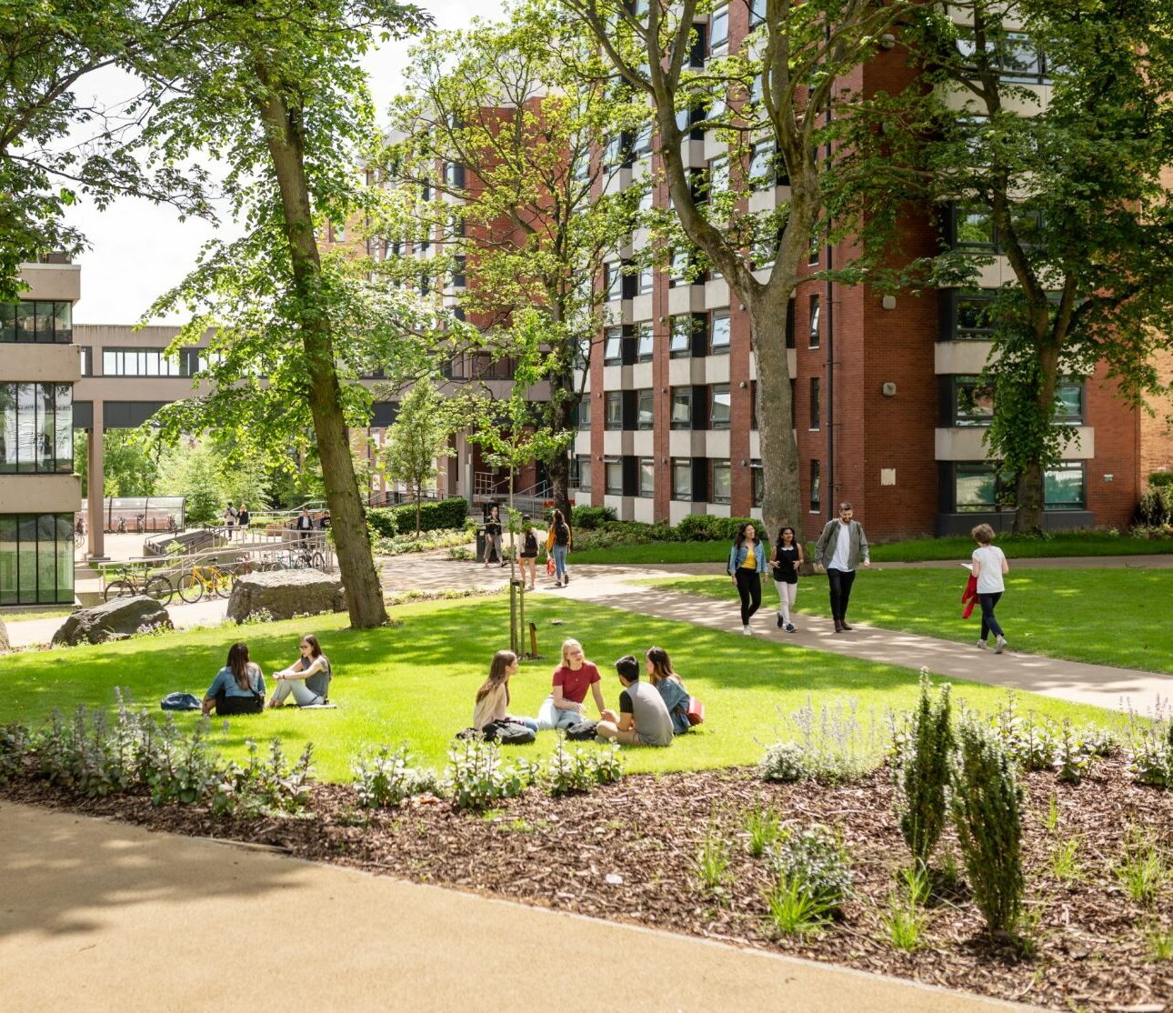 A university campus with students walking and sitting on grass on a sunny day.