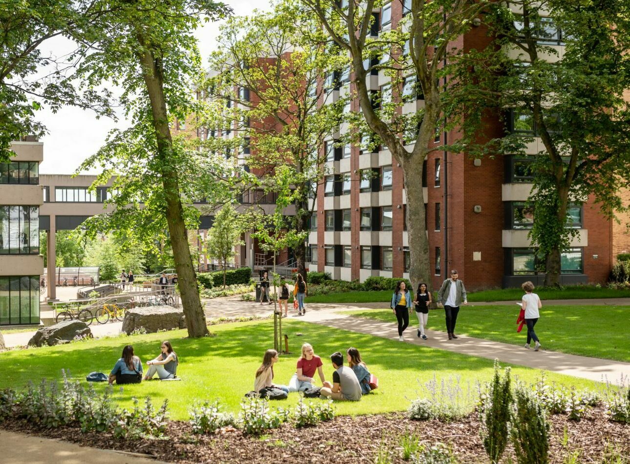 A university campus with students walking and sitting on grass on a sunny day.